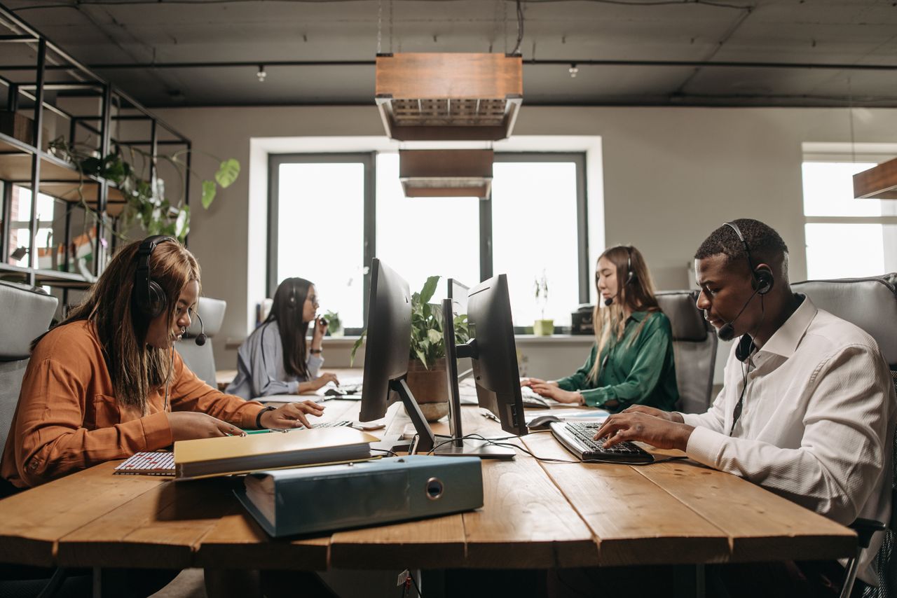 Home A diverse group of employees collaborating with headsets in a modern office setting.