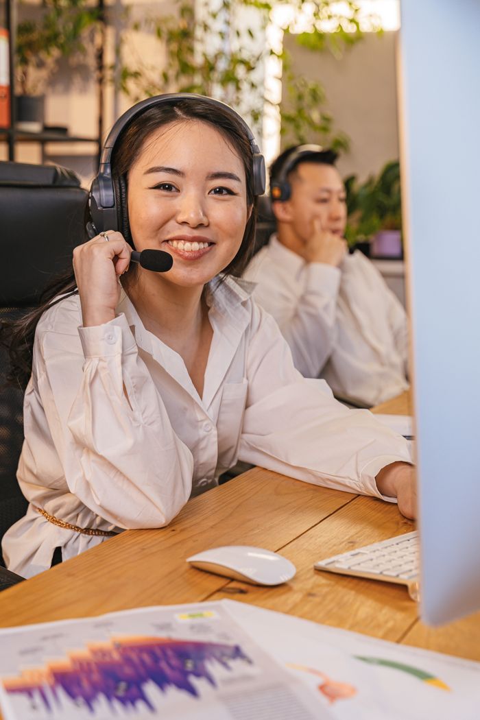 About Smiling employees at call center desk using headsets and computers.