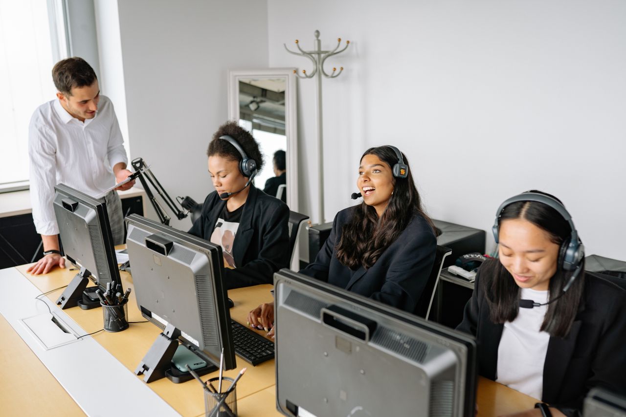 Home A diverse team of customer service representatives working in an office setting, wearing headsets and using computers.